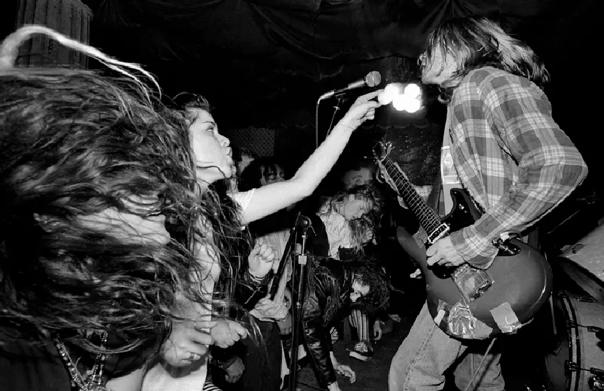 An old black and white photo of Kurt Cobain of Nirvana playing and singing in front of a crows.