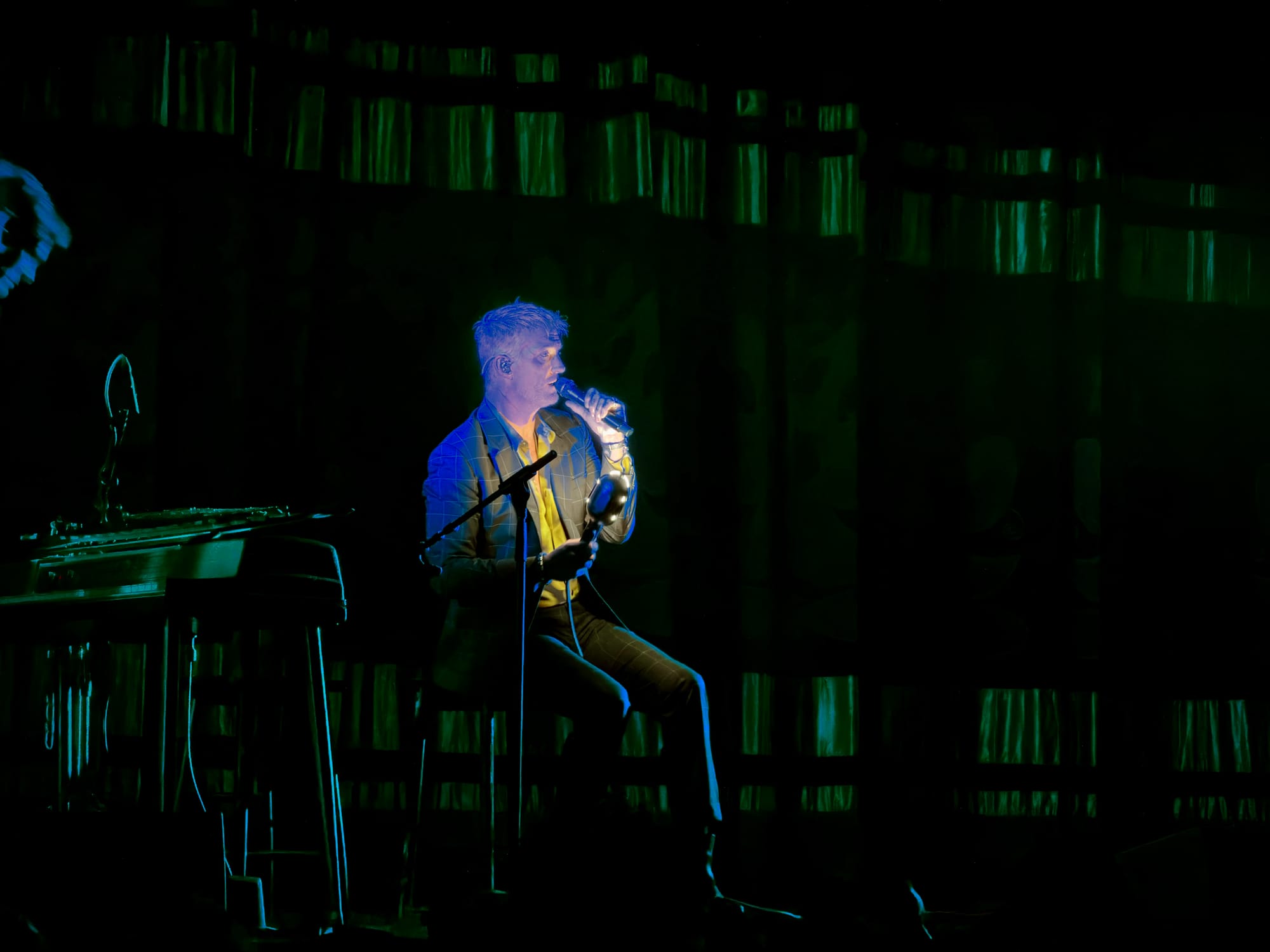 Josh Homme sitting on a stool, singing into a microphone.